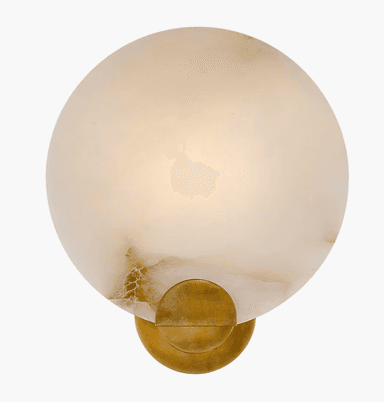 A modern wall sconce featuring a circular, translucent natural stone diffuser with subtle veining, mounted on a compact, brushed brass base. The light is emitted softly and diffusedly through the stone. — 3D model