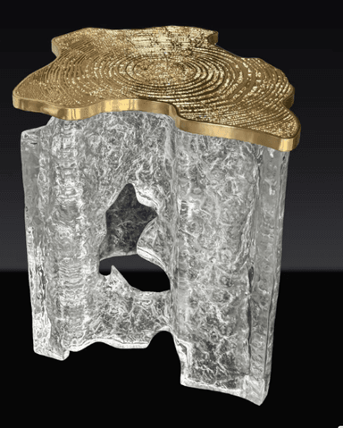A striking coffee table featuring an irregular, organic-shaped tabletop made of polished golden brass, adorned with a detailed concentric ring pattern. The base is crafted from a chunky, translucent material, likely clear resin or acrylic, sculpted into an abstract, ice-like form, creating a visually compelling contrast with the metallic top. The table exhibits a low profile. — 3D model