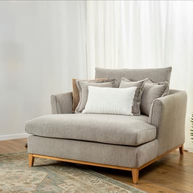 A contemporary chaise lounge featuring light gray fabric upholstery, a deep seat, and a low-profile backrest. It is supported by a minimalist exposed wooden frame with short, splayed legs. The chaise comes with multiple loose back cushions and a small white decorative pillow. — 3D model