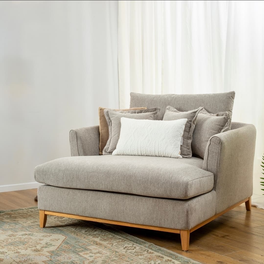 A contemporary chaise lounge featuring light gray fabric upholstery, a deep seat, and a low-profile backrest. It is supported by a minimalist exposed wooden frame with short, splayed legs. The chaise comes with multiple loose back cushions and a small white decorative pillow. — 3D model