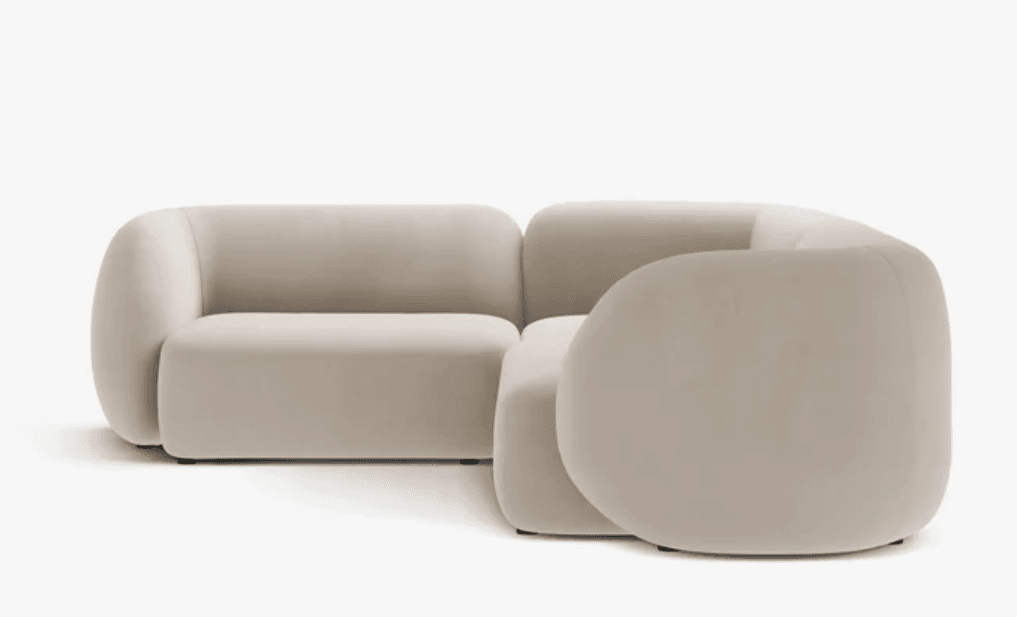 A modular, light beige sectional sofa with rounded edges and a soft, upholstered finish. It features a corner configuration with two distinct modules, one appearing to be a corner seat and the other an armless or low-arm section. The design is minimalist and contemporary, with a focus on plush comfort and organic shapes. The sofa is presented against a plain white background. — 3D model