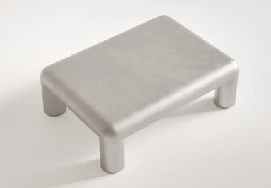 A contemporary coffee table with a monolithic design. It features a rectangular top with rounded edges that seamlessly transitions into four cylindrical legs. The overall form is smooth and sculptural, suggesting a modern aesthetic. — 3D model