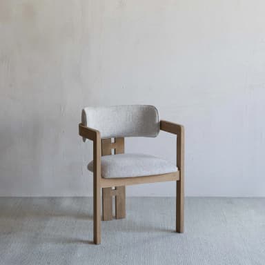 A contemporary dining chair featuring a light-toned wooden frame and light gray upholstered seat and backrest. The backrest is gently curved, providing integrated armrests as part of the overall wooden structure. The rear legs feature distinctive H-shaped vertical cutouts, adding to its modern aesthetic. — 3D model