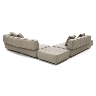 A contemporary sectional sofa with a chaise lounge. The sofa features a light beige or cream-colored upholstery with subtle stitching details creating a segmented appearance on the seating and back cushions. It includes two accent throw pillows in a similar neutral tone. A section of the sofa incorporates a light-colored, possibly marble or stone, tabletop integrated into its structure. The sofa is presented on a black background. — 3D model