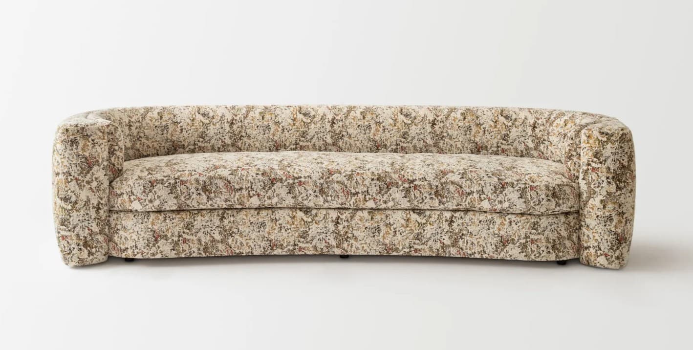 A curved sofa upholstered in a textured fabric with an abstract pattern. The sofa features rounded arms that seamlessly integrate into the backrest, creating a continuous, organic form. The seat is composed of a single cushion, and the backrest is also a continuous curve. The upholstery displays a mélange of colors including cream, beige, brown, and subtle hints of red and green. — 3D model
