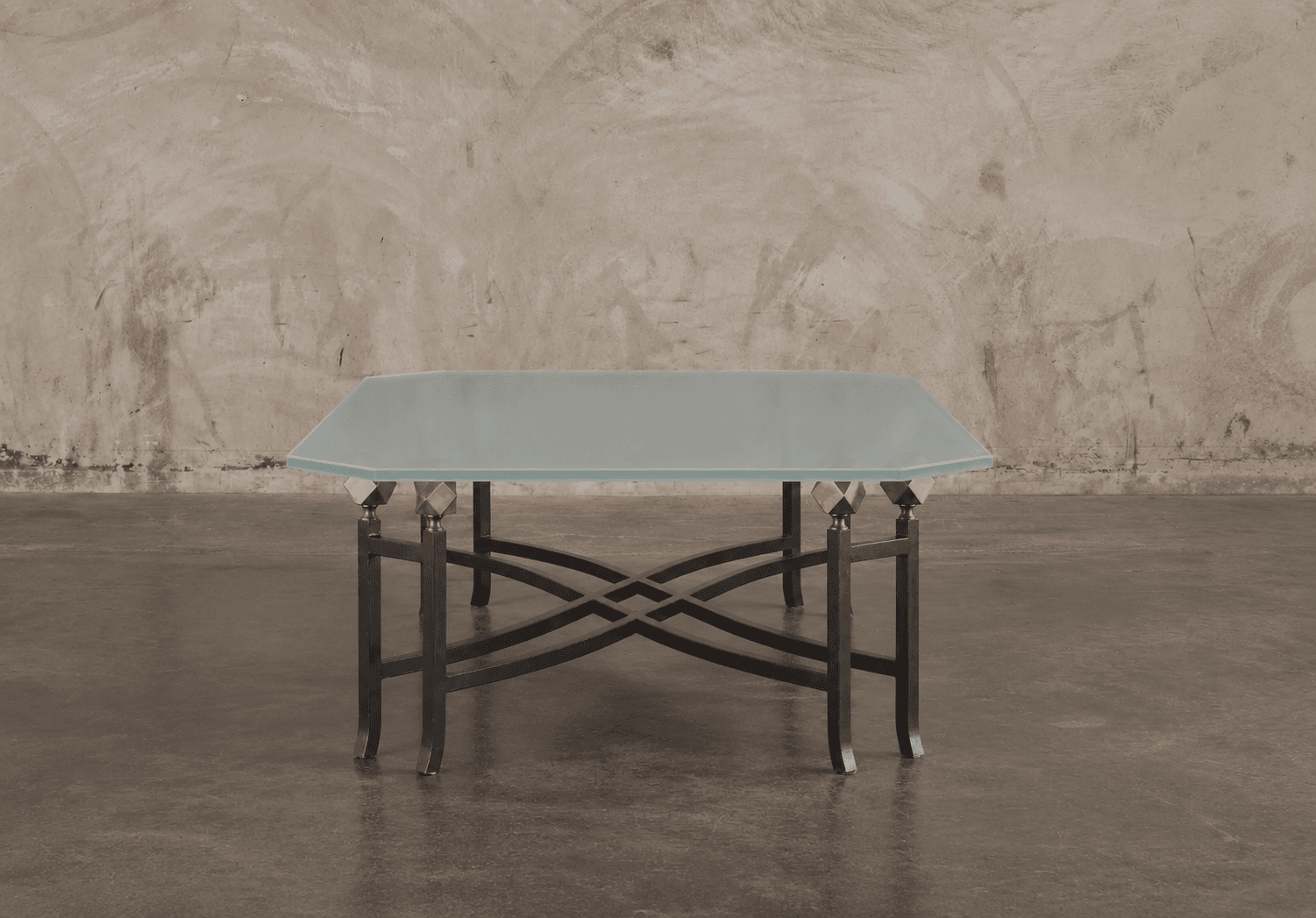 A low-profile table featuring a frosted glass top with an octagonal shape, supported by a wrought iron base with intricate curved and intersecting elements. Decorative brass finials connect the glass top to the metal base. — 3D model