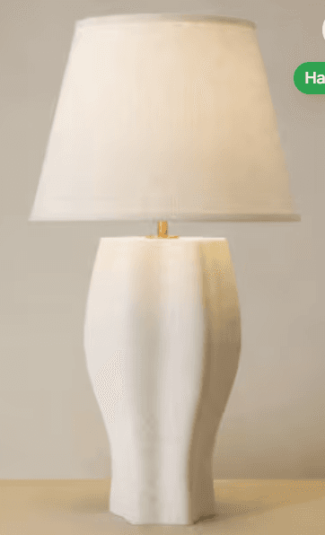A modern table lamp featuring a sculptural, fluted ceramic base in a matte white finish, topped with a complementary tapered fabric lampshade. A small brass finial is visible between the base and the shade. — 3D model