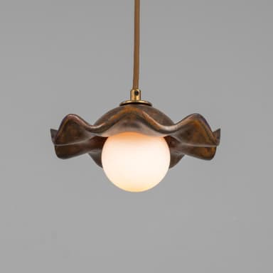 A pendant light featuring a distinctive wavy, shell-like metal shade with a mottled, patinated bronze finish. Suspended beneath the shade is a spherical frosted glass diffuser, emitting a soft, warm light. The fixture hangs from a braided textile cord, connecting to the shade via a small brass fitting. — 3D model