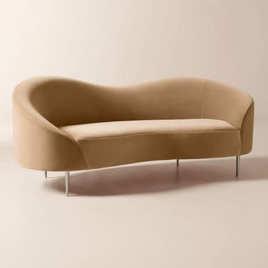 A modern curved back sofa upholstered in plush, champagne-colored velvet, featuring slender, polished stainless steel legs with a champagne finish. — 3D model