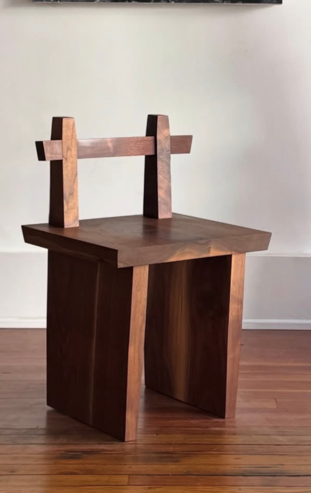 A minimalist low chair constructed from dark, solid wood, featuring a thick, rectangular seat and a backrest composed of two vertical posts supporting a single horizontal bar. The base consists of two sturdy, panel-like legs, giving it a robust, blocky appearance. — 3D model