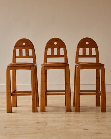 A wooden bar stool featuring a natural finish, a slatted backrest with an arched top rail, a circular cut-out, and integrated footrests on all four sides. — 3D model