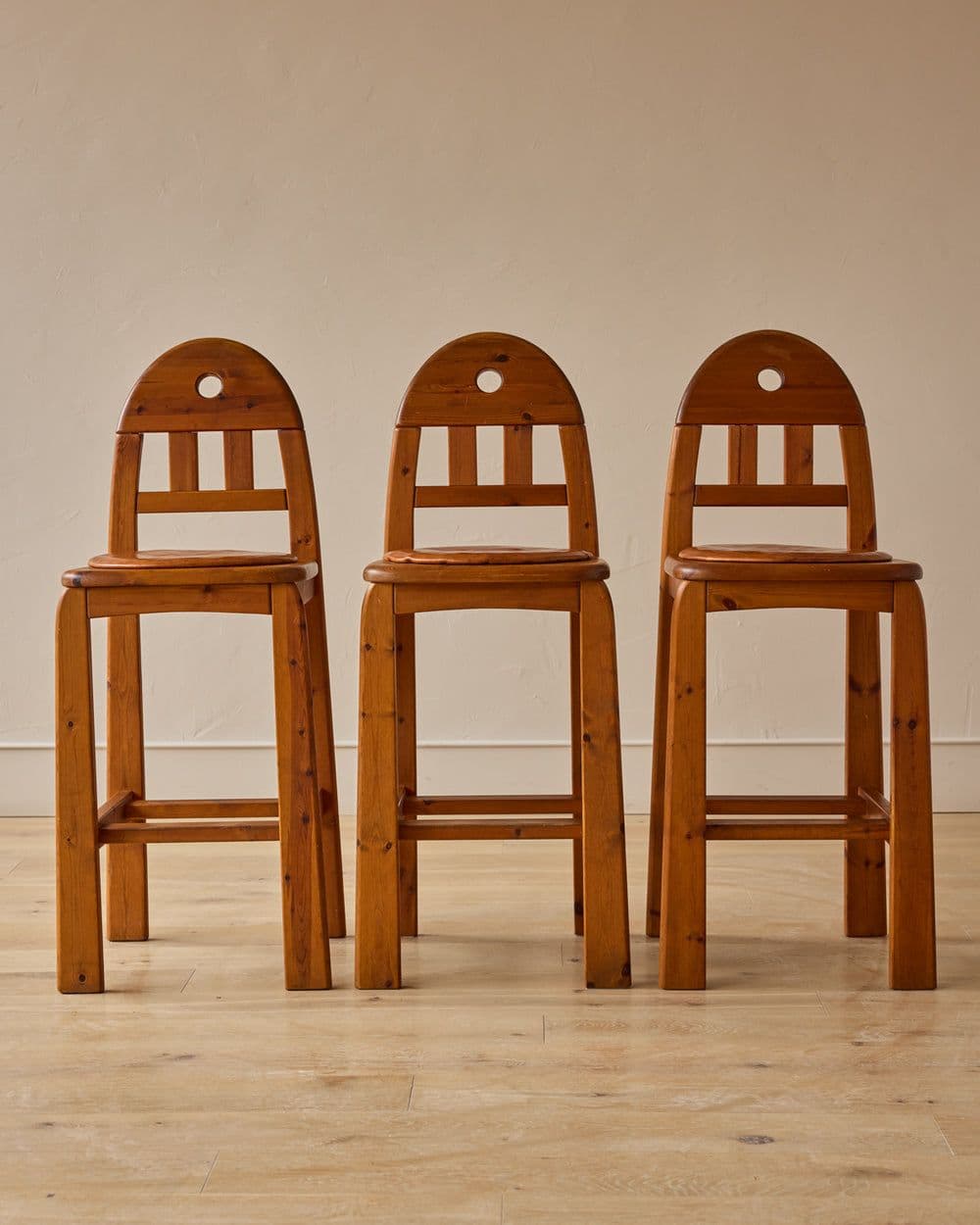A wooden bar stool featuring a natural finish, a slatted backrest with an arched top rail, a circular cut-out, and integrated footrests on all four sides. — 3D model