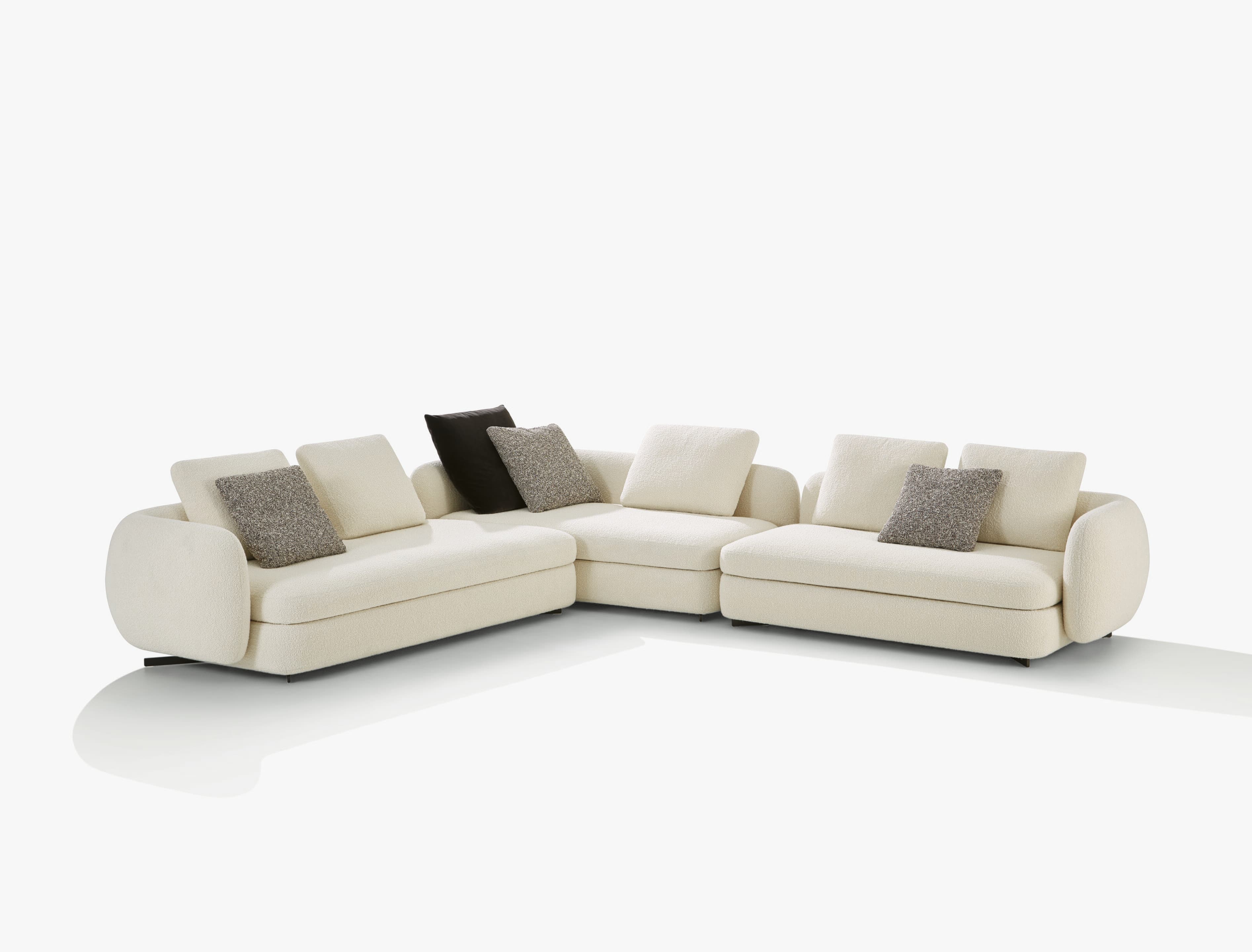 A contemporary L-shaped sectional sofa upholstered in a light cream-colored boucle fabric, featuring thick, plush cushions and rounded armrests and backrests. The sectional includes several decorative pillows, some matching the main upholstery and others in contrasting gray textured and black solid fabrics. — 3D model