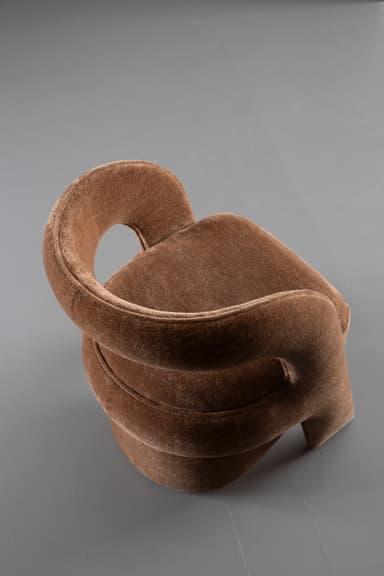 A contemporary sculptural accent chair fully upholstered in a textured medium brown fabric, featuring a continuous, curvilinear backrest and armrests that flow seamlessly into an integrated, upholstered cylindrical base. — 3D model