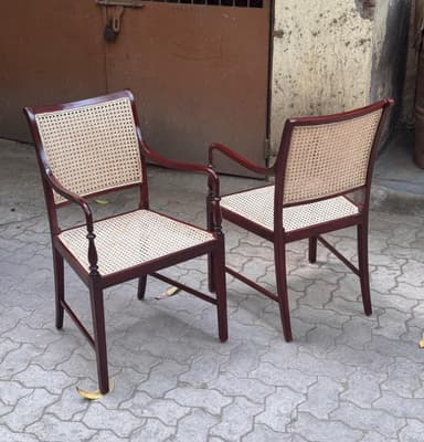 A classic colonial-style armchair featuring a dark-stained wooden frame with a cane woven seat and backrest. The armrests are gently curved, supported by elegantly turned spindles, and the legs are straight. — 3D model