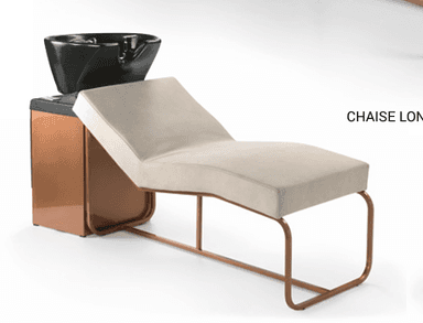 This image features a modern salon shampoo unit designed for professional hair washing services. It consists of a long, upholstered chaise-style reclining bed with a light beige or cream-colored cushion, supported by a continuous tubular metal frame with a copper-toned finish. At one end, there is a compact cabinet-like structure, also with a copper-toned metallic finish, which integrates a glossy black ceramic or plastic shampoo basin. The basin includes an indented area for neck support, suggesting it is a fixed unit for client comfort during hair washing. The overall design is sleek and contemporary. — 3D model