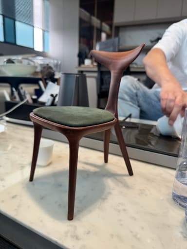 A modern dining chair with a curved wooden frame and a padded seat. The chair features a distinctive, wing-shaped backrest that extends upwards and outwards. The seat is upholstered in a dark green fabric, contrasting with the rich, dark wood of the frame. — 3D model