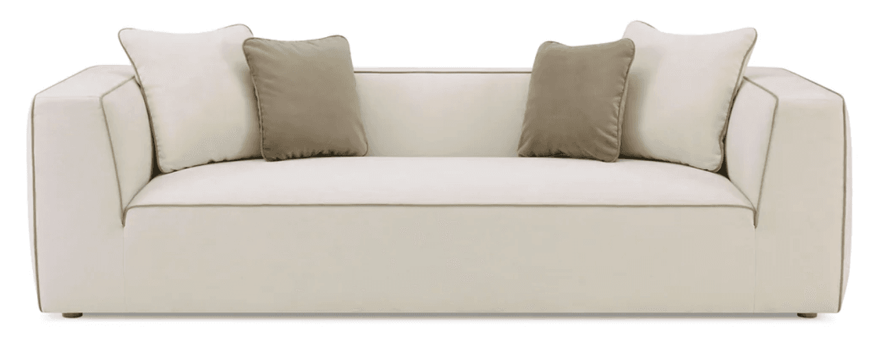 A modern, upholstered sofa with a clean, angular design. It features a low profile, squared arms, and a deep seat. The upholstery is a light cream color, accented with a subtle contrast piping in a darker tone along the edges of the cushions and frame. Two throw pillows are included, one in a light cream and another in a taupe color, both with a soft texture. — 3D model