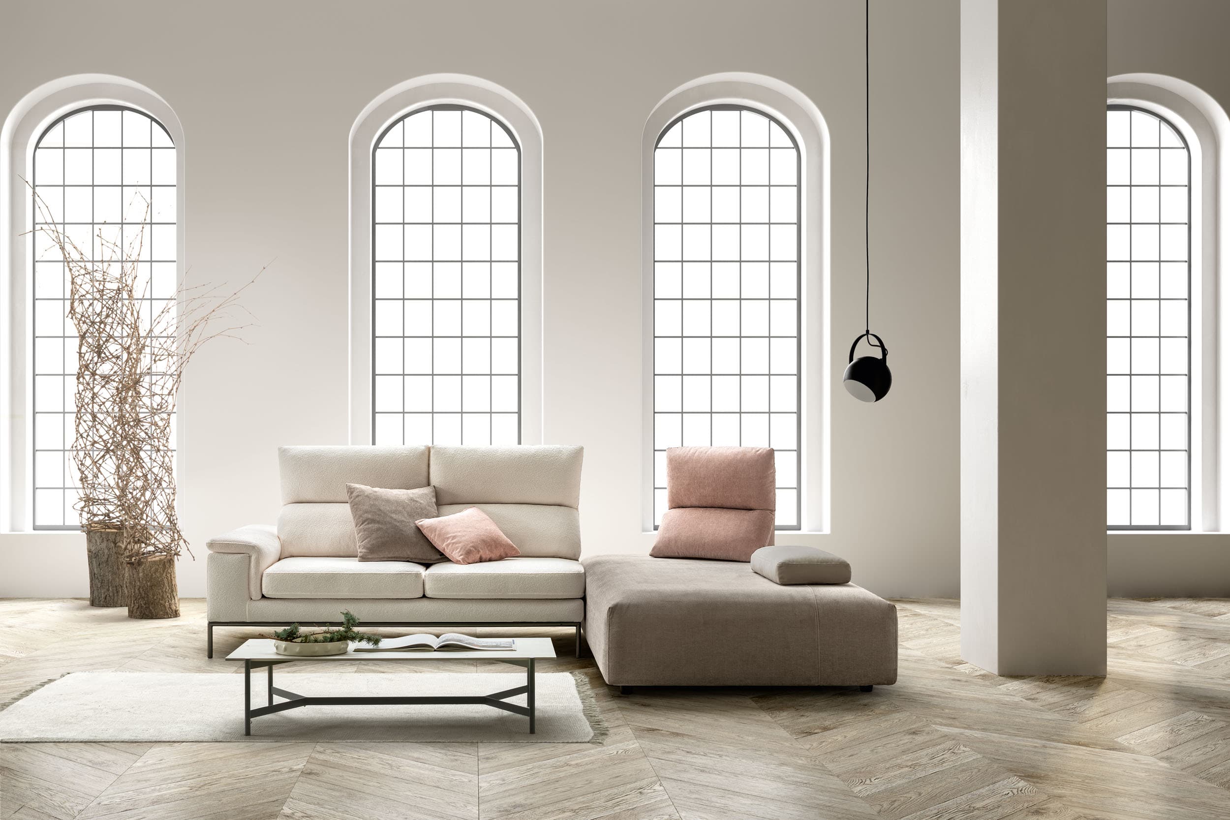 A modular sectional sofa with a left-arm facing chaise lounge. The sofa features a light-colored, textured fabric upholstery on the main seating sections and backrests. It includes adjustable headrests on the main sofa section and several throw pillows in varying shades of pink and grey. The chaise lounge section is upholstered in a taupe, textured fabric and has a low profile. The base of the sofa section is supported by slender black metal legs, creating a modern aesthetic. — 3D model