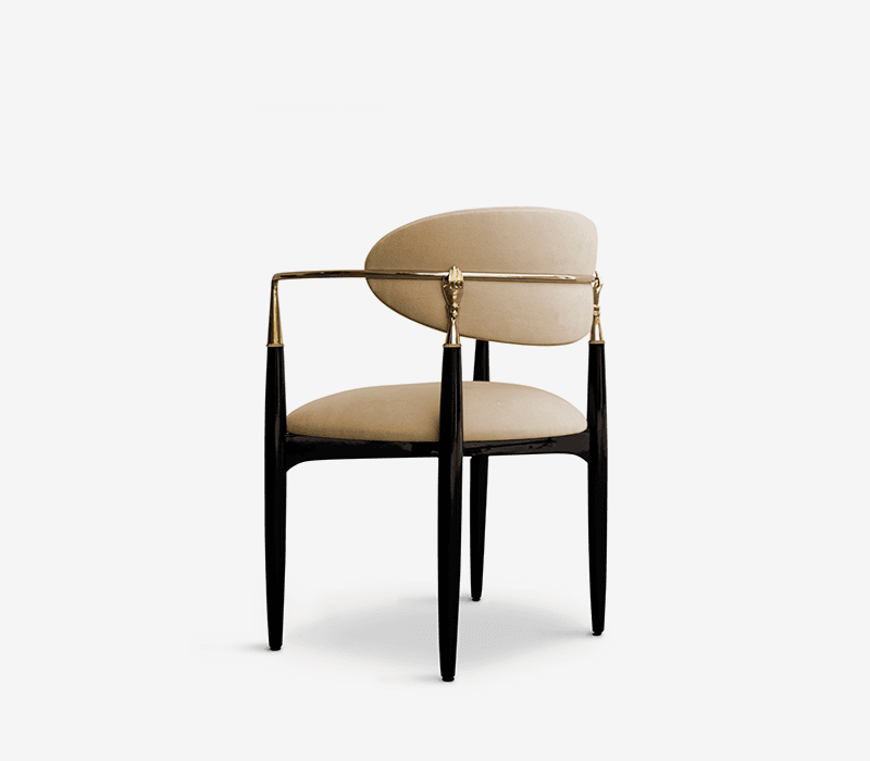 A sophisticated armchair with a curved, upholstered backrest and seat, supported by four legs. The chair features armrests with a sleek metallic finish and decorative, ornate gold-colored embellishments at the points where the armrests connect to the backrest. The legs are slender and tapered, finished in a high-gloss black. — 3D model