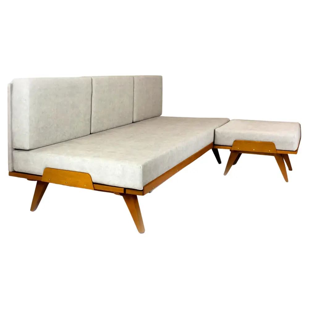 A Mid-Century Modern style daybed featuring a light-toned wooden frame and light grey fabric upholstery, accompanied by a matching, separate ottoman. — 3D model