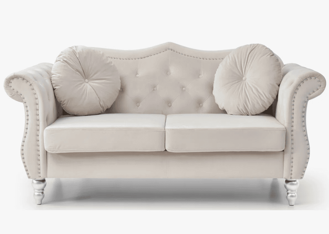An elegant tufted chaise lounge featuring a high, curved backrest and a single scrolled armrest, upholstered in a light beige or cream fabric. The piece is characterized by deep button tufting on the back and inner arm, and decorative nailhead trim along the edges of the back, arm, and base. It has two removable seat cushions and includes two round, tufted bolster pillows. The chaise rests on four short, ornate silver-finished legs. — 3D model
