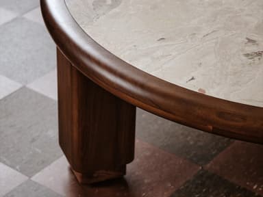 A low, round coffee table featuring a light-colored natural stone top, likely travertine, set within a thick, rounded frame of dark wood. The table is supported by four robust, chunky cylindrical wooden legs. — 3D model