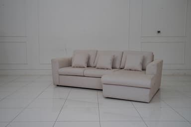A sectional sofa with a chaise lounge extension, upholstered in a light-colored fabric with a subtle pattern. The sofa features three seat cushions and a chaise on the right side. It includes four matching throw pillows. The sofa has a modern, minimalist design with clean lines and low-profile arms and back. — 3D model