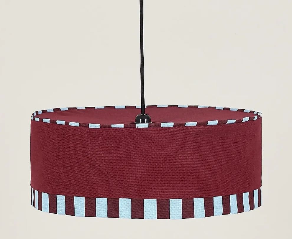 A contemporary drum-shaped pendant light featuring a main body crafted from burgundy-colored fabric. The top and bottom edges of the cylindrical shade are adorned with a decorative textile trim, showcasing a pattern of alternating light blue and dark burgundy vertical stripes. The fixture is suspended by a black electrical cord. — 3D model