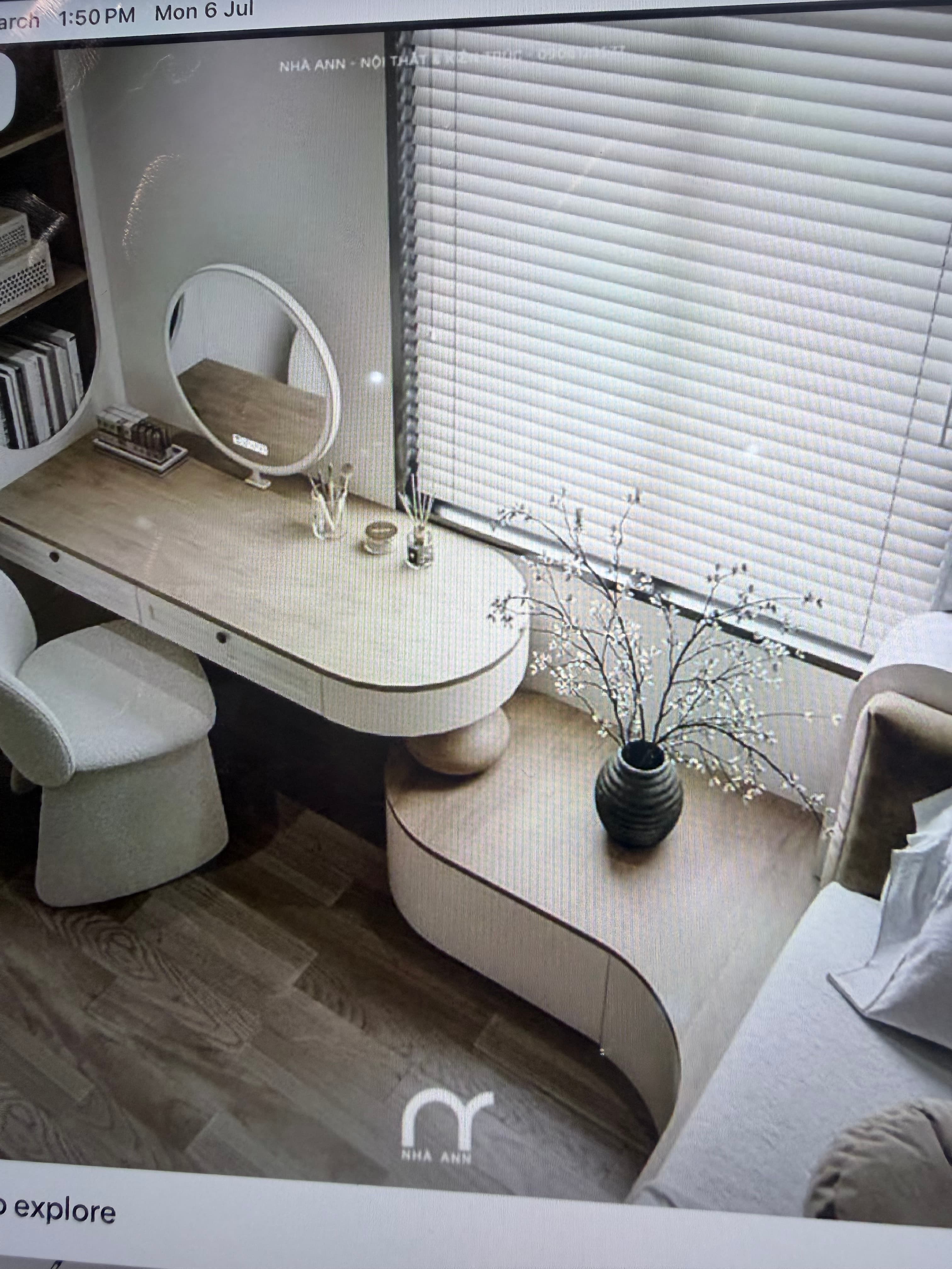 A contemporary vanity desk constructed from light-toned wood, featuring an organic and curved design. It includes a movable circular mirror with what appears to be integrated lighting, and multiple hidden drawers for storage. The table surface is split into two sections, one with the mirror and drawers, and another lower, wavy section for display or additional surface area. — 3D model