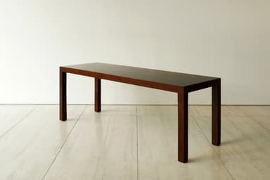 A long, narrow, dark brown console table with a minimalist design, featuring a rectangular top and four straight, thick legs integrated seamlessly into the corners, resting on a light tiled floor. — 3D model