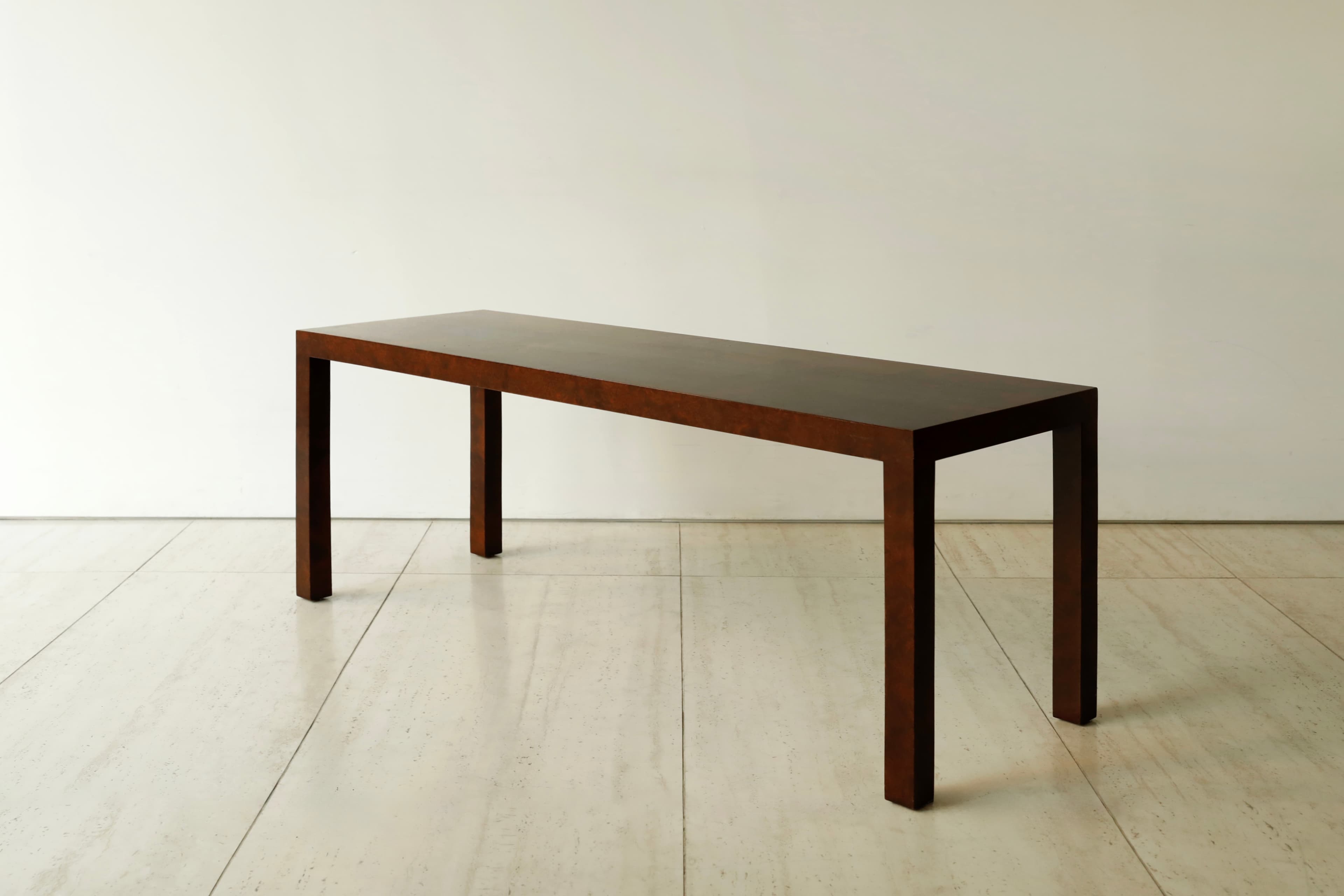 A long, narrow, dark brown console table with a minimalist design, featuring a rectangular top and four straight, thick legs integrated seamlessly into the corners, resting on a light tiled floor. — 3D model