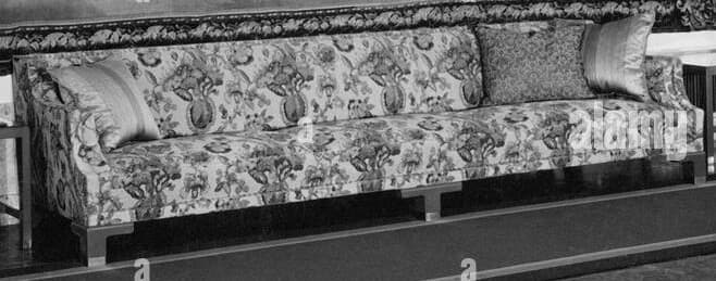 A long upholstered sofa with a floral pattern fabric covering its cushions, backrest, and frame. It features two decorative throw pillows. The sofa has a slightly ornate design with visible wooden legs and armrests. The upholstery has a detailed botanical motif. — 3D model