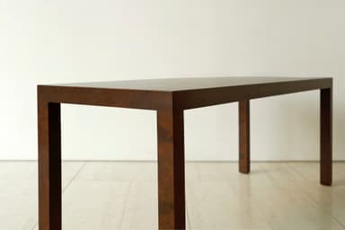 A long, narrow, dark brown console table with a minimalist design, featuring a rectangular top and four straight, thick legs integrated seamlessly into the corners, resting on a light tiled floor. — 3D model