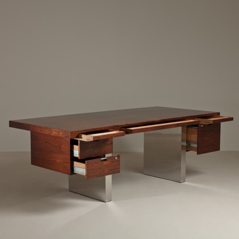A large, executive desk with a dark wood veneer top and sides. It features multiple drawers, some of which are open, revealing wooden interiors and metal drawer slides. The desk is supported by two substantial, brushed metal pedestals. The overall design appears modern and functional. — 3D model