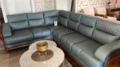 An L-shaped sectional sofa upholstered in dark gray leather, featuring distinct quilted headrests with diamond stitching. The sofa incorporates visible wooden panels on the outer sides of the armrests and a wooden base frame supported by tapered wooden legs. It has a modern aesthetic with clean lines and plush cushioning. — 3D model