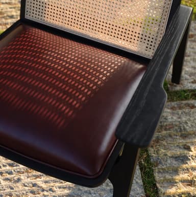 A modern armchair with a dark wood frame and cane back. The seat is upholstered in black material, likely leather or faux leather. The frame has clean lines, with angled legs and armrests. — 3D model