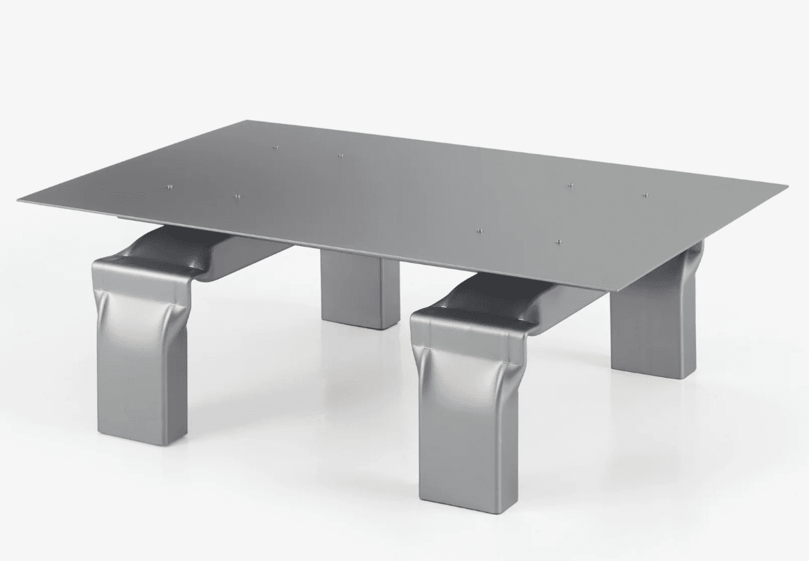 A modern coffee table with a rectangular, flat, metallic surface. The tabletop is supported by four distinct legs. Two of the legs are straight and rectangular in profile, while the other two have a more sculptural, curved design where they meet the tabletop and then transition to a straight, rectangular base. The legs appear to be constructed from the same metallic material as the top, giving it a cohesive and minimalist aesthetic. — 3D model