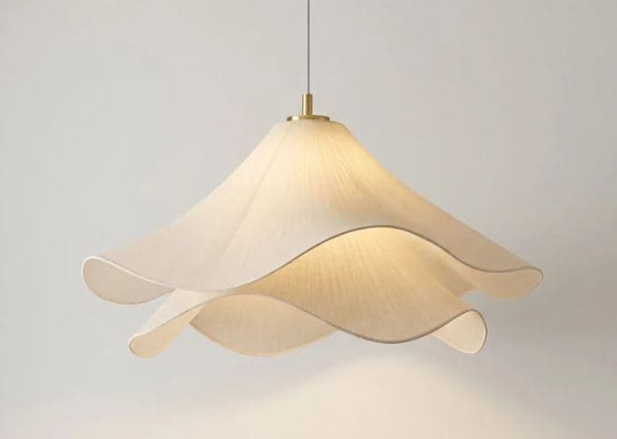 A contemporary pendant light featuring a shade crafted from multiple layers of off-white fabric, arranged in a petal-like, sculptural form. The layers overlap and gently curve outwards, creating a soft, diffused light effect. The light fixture is suspended by a white cord, which connects to a small, cylindrical brass accent at the top of the shade. — 3D model