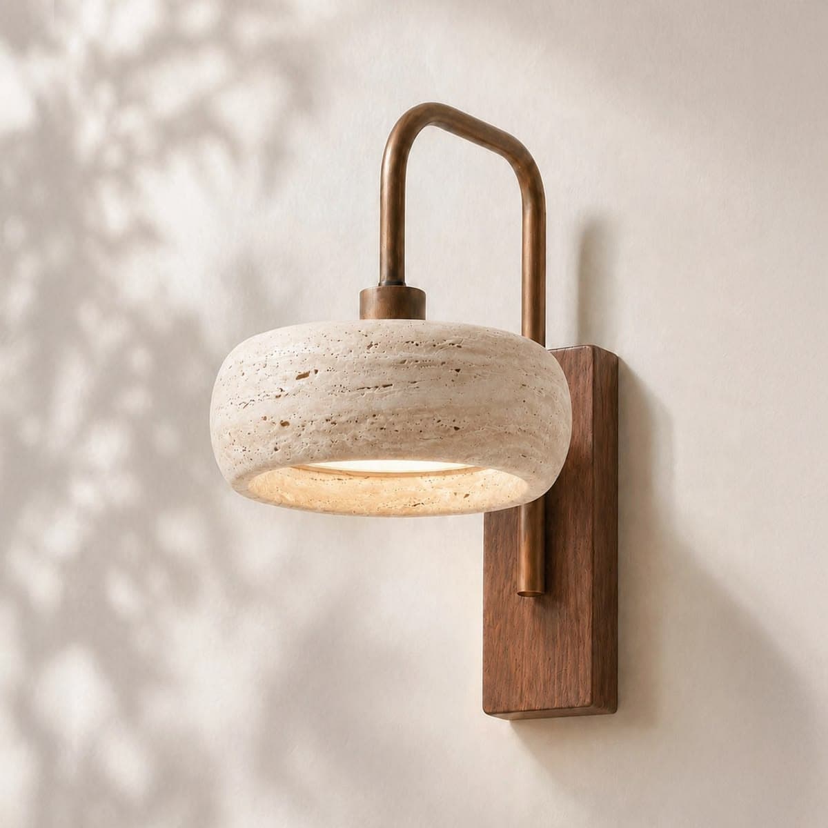 A modern wall sconce featuring a bowl-shaped shade crafted from rough-textured travertine stone. The shade emits a soft, diffused light. It is supported by a curved, aged brass arm that attaches to a rectangular wooden backplate, which is designed for wall mounting. — 3D model