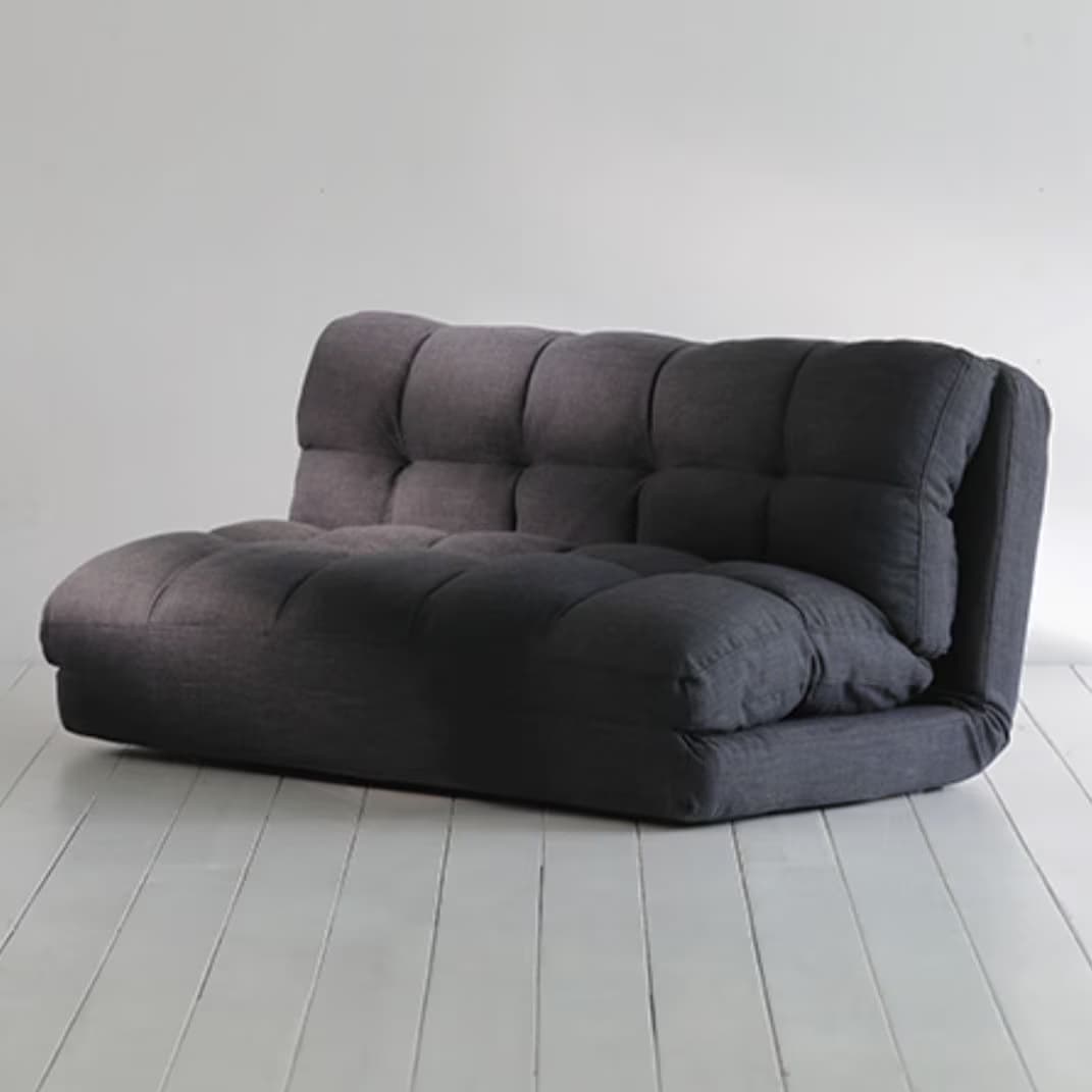 A contemporary, floor-level futon sofa designed for versatility and comfort, upholstered in a dark gray tufted fabric. It features a segmented design that allows for an adjustable backrest, suggesting functionality as both a seating option and a reclining or sleeping surface. The cushioning is substantial, providing a plush appearance. Its compact, legless form factor makes it suitable for various living arrangements. — 3D model