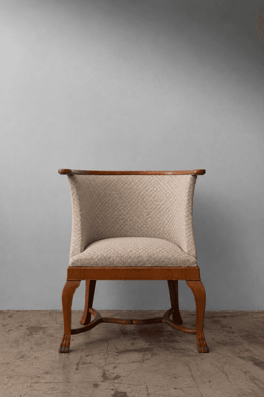 A refined barrel-back armchair featuring a solid wood frame with a polished light brown finish. The chair's back and seat are upholstered in a textured beige fabric with a distinctive diamond quilting pattern. The continuous back curves gracefully to form integrated, low-profile armrests. The chair is supported by four tapered, carved wooden legs, connected by an elegant stretcher base. — 3D model