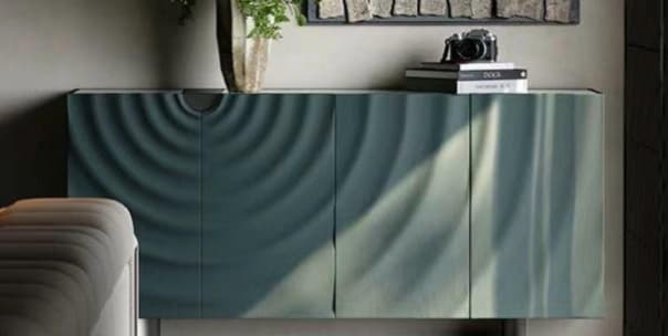 A contemporary long, rectangular storage cabinet or sideboard featuring four doors with a distinctive embossed ripple or wave pattern across their surfaces. The cabinet is finished in a dark teal or petrol blue color. — 3D model