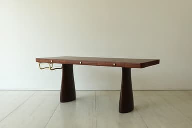 A sleek, dark brown executive desk featuring a substantial rectangular top supported by two wide, tapering sculptural pedestal bases, accented with brass details and integrated drawers. — 3D model