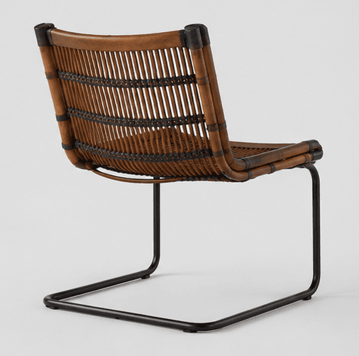 An armless lounge chair featuring a natural rattan or cane seat and backrest with a tubular black metal sled base. The woven material is a warm brown tone, secured to a bent rattan frame, which is then attached to the minimalist metal frame. The design presents a relaxed and contemporary aesthetic. — 3D model
