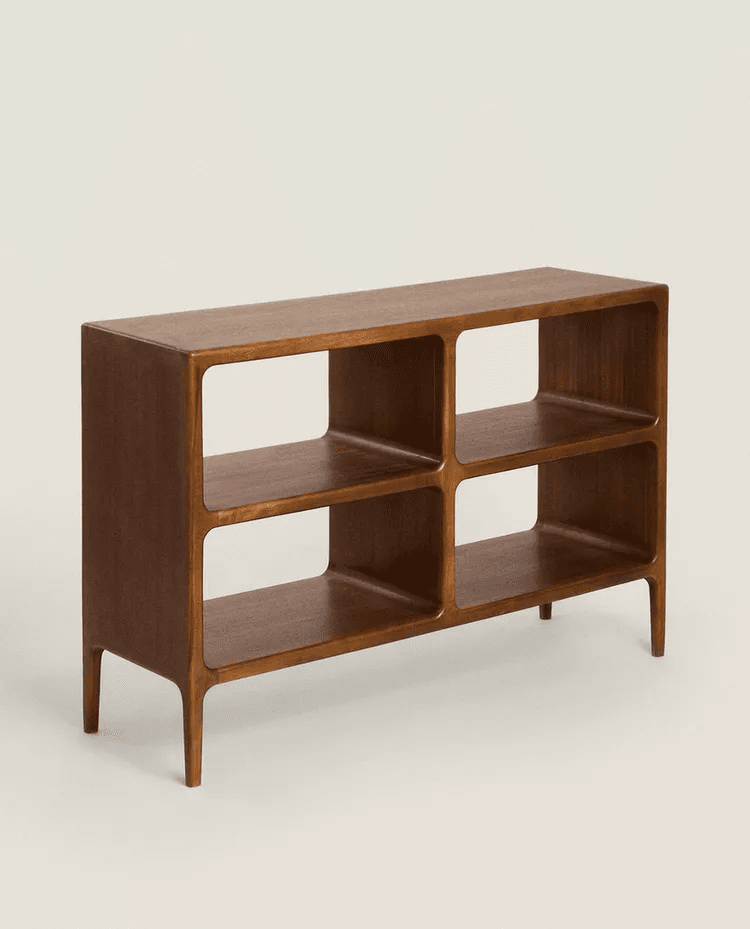 A low, rectangular bookshelf with an open design. It features a smooth, finished wooden surface and is divided into four cubby-like compartments by horizontal and vertical dividers. The unit is supported by four tapered legs, two at the front and two at the back, which are slightly splayed. — 3D model