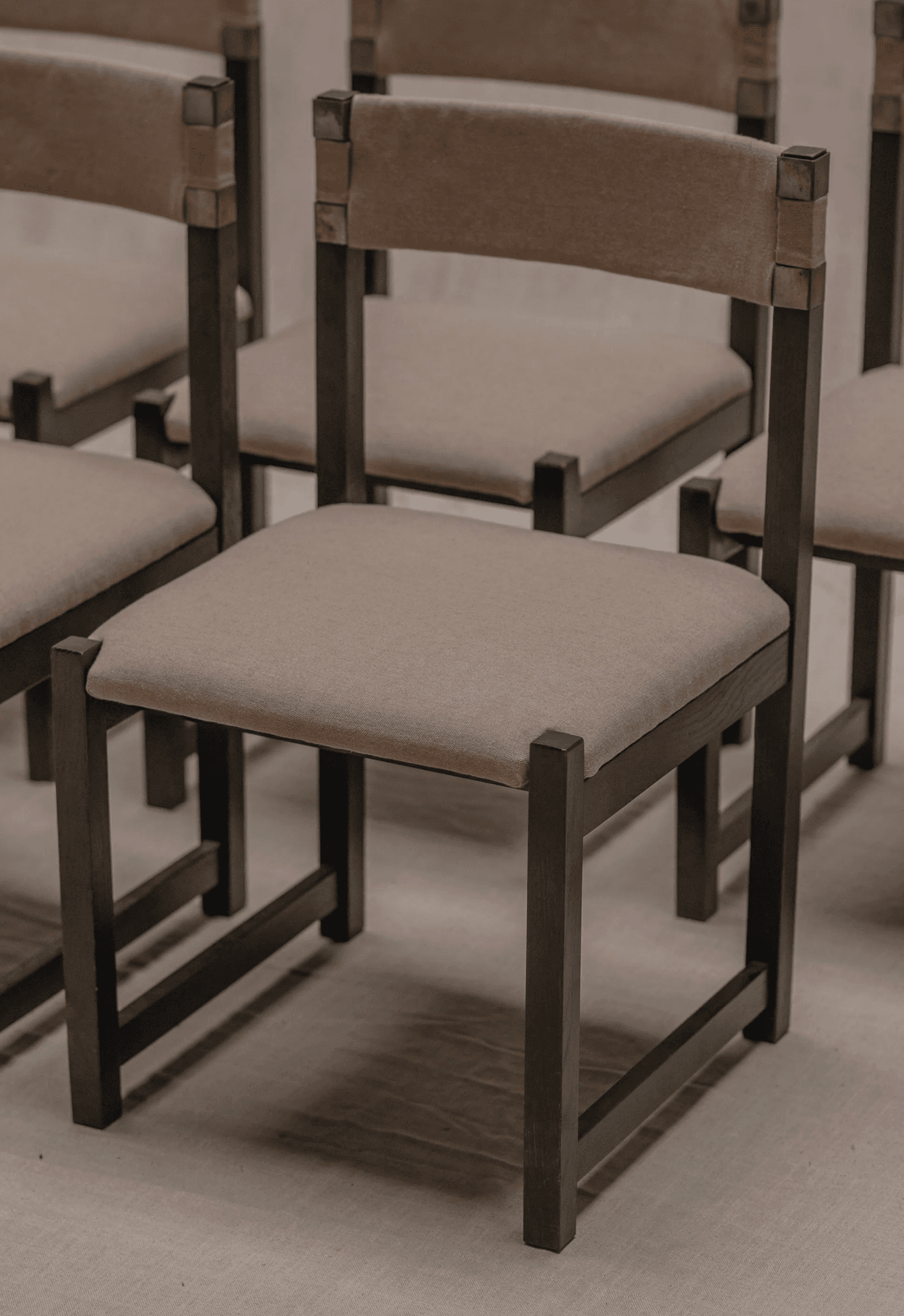 A contemporary chair with a dark metal frame and upholstered seat and back. The frame has a minimalist design with straight lines. The seat and back are upholstered in a light brown fabric. Metal brackets connect the upholstered backrest to the vertical supports of the frame. — 3D model