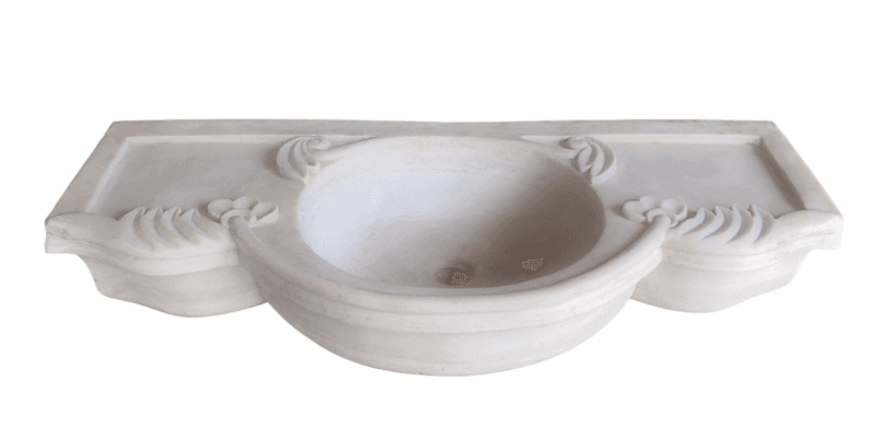 A wall-mounted sink basin with an integrated countertop and decorative carving. The basin is circular with a smooth, sloped interior leading to a central drain opening. The countertop extends horizontally on either side of the basin, with a raised edge. The front of the sink features a decorative curved apron with elaborate floral and scroll carvings. — 3D model