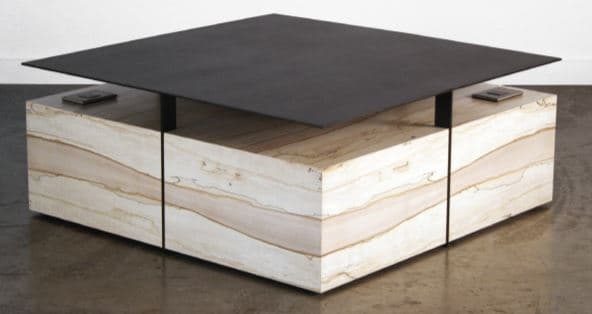 A contemporary coffee table with a distinctive design. It features a thin, square, matte black top that appears to be made of metal or stone. This top is supported by minimalist black metal legs. The base of the table is a substantial, block-like structure constructed from layered stone or marble, exhibiting prominent horizontal banding in shades of cream, beige, and light brown, creating a geological strata effect. The base is divided into two segments by a vertical seam. — 3D model