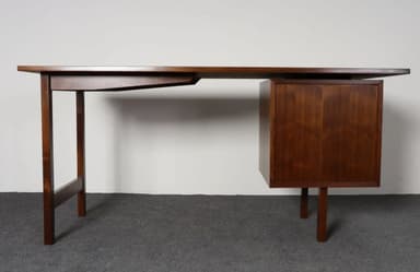A vintage Mid-Century Modern wooden executive desk featuring a dark brown finish. The desk comprises a broad rectangular tabletop supported by two slim, square-profile legs on one side, connected by a stretcher bar. The opposite side features a cantilevered or 'floating' rectangular drawer pedestal, supported by two shorter, slightly splayed legs. The design emphasizes clean lines and a minimalist aesthetic typical of the era. — 3D model